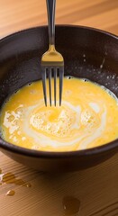 Whisking Raw Eggs and Creamy Milk in a Dark Preparation Bowl for Cooking.