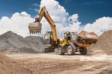 A loader transports sand from the ground to a storage bin at a construction site. An excavator...