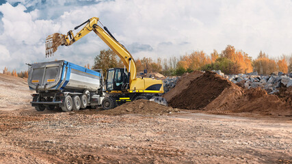 Obraz premium Construction workers use a loader and excavator to move dirt and materials at a site with trees and rocks in the background during daytime