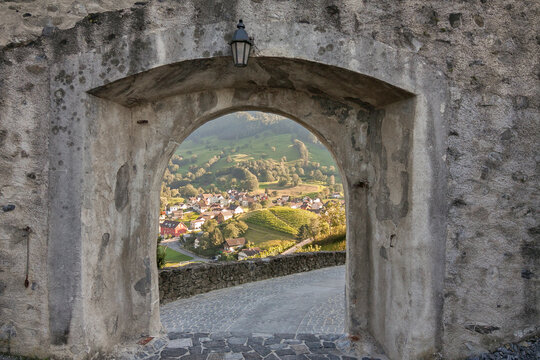 The view through the stone gate under the antique lamp across the green valley towards the nice tiny town and hilly vineyard. Balzers, Liechtenstein