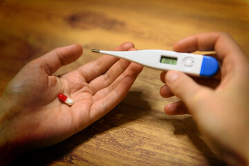 Closeup Hands Holding Antiviral Pill and High Fever Thermometer