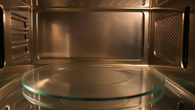 Interior view of a metallic, illuminated oven featuring a glass plate. Grid and ventilation detailing. Reflections and symmetry create an interesting perspective