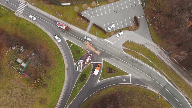 Firefighters cleaning an oil spill after a car crash at a road intersection in Slovenia, with emergency vehicle managing traffic and safety, top-down view