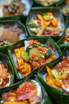 Close up of traditional Indonesian side dishes with chili sauce served in banana leaf cups. Authentic Asian street food with natural packaging and rich textures.