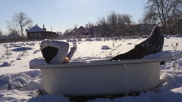 Creative winter lifestyle shot: a woman lies in an open-air bathtub amidst the snow, holding a glass of snow in the form of a cocktail