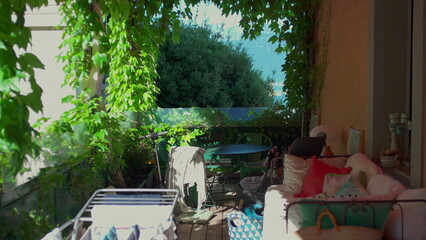 Naklejka premium Shaded garden balcony with cozy furniture, climbing plants, drying rack and mountain view in background, peaceful domestic outdoor space on sunny summer day