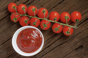 Fresh cherry tomatoes on vine next to bowl of rich, red tomato sauce on rustic wooden surface, creating vibrant and appetizing scene