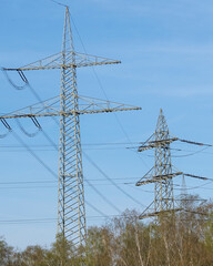 High voltage power lines are visible against a clear blue sky in an open area surrounded by trees during daytime