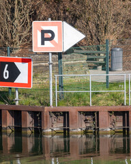 Parking sign and directional arrow near the water at a public park area with a walking path and green space
