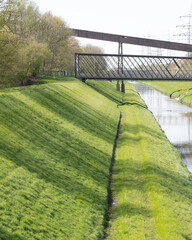 Bridge crossing over a green riverbank with trees and light reflections in the water during daytime near a city