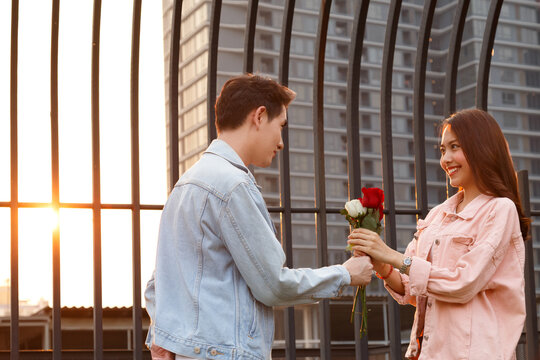young happy couple love and romantic at first date relationship. asian teenage woman surprise and smiling at boyfriend gives red rose flowers at dinner in valentine day. couple and happiness concept.