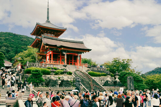 Crowd of tourists visiting the Kiyomizu dera temple with its iconic red pagoda under a cloudy sky in the hills of Kyoto Japan