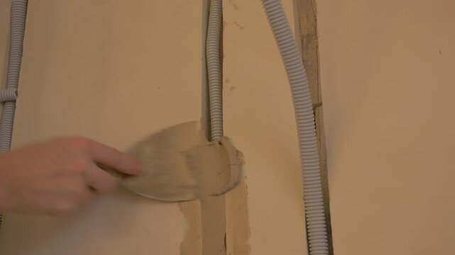 Electrician applying plaster to wall with visible electrical wiring and tools in a residential construction setting. electrician man. Build house man