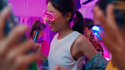 Closeup group multiethnic young adult Asia friend wear futuristic neon glowing glasses dance and drink alcohol beer fun hangout party in living room night indoor home. Disco lights illuminating house.