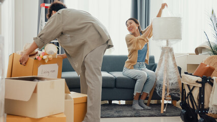 Young happy Asian couple help each other moving box full of stuff unpacking furniture on sofa couch in living room at new house. Husband and wife move new house, Apartment Rent And Ownership Concept.