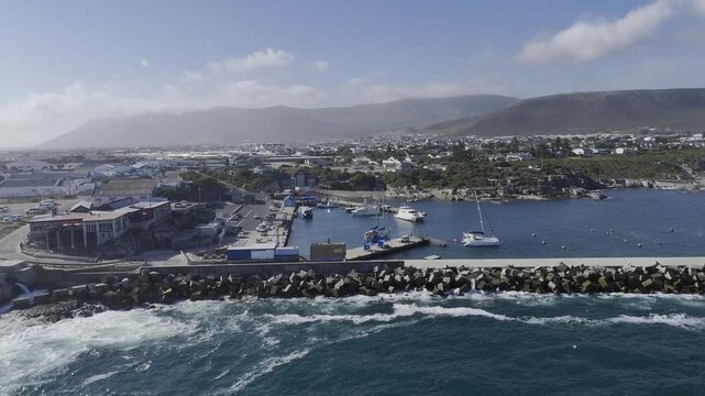 Drone flies to the left along the new harbor and orbits around the abalone farm on sunny day in Hermanus on the Garden Route in South Africa