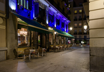 Obraz premium Cozy old street with table of restaurant in Madrid, Spain. Architecture and landmark of Madrid. Night cityscape of Madrid.