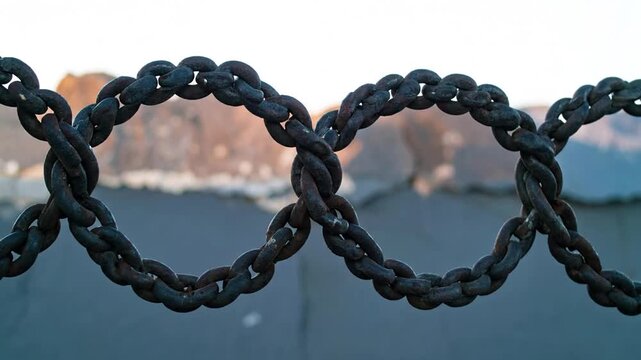 Close-up of intertwined chain links against a blurred backdrop of stone and sky