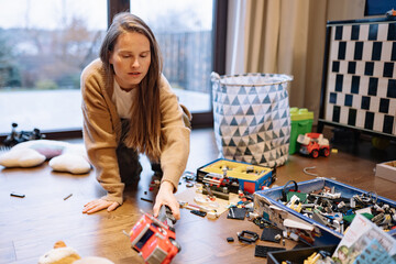 Woman cleans room after her child plays with toys on the floor and leaves a mess at home during a rainy day © yaaaaan