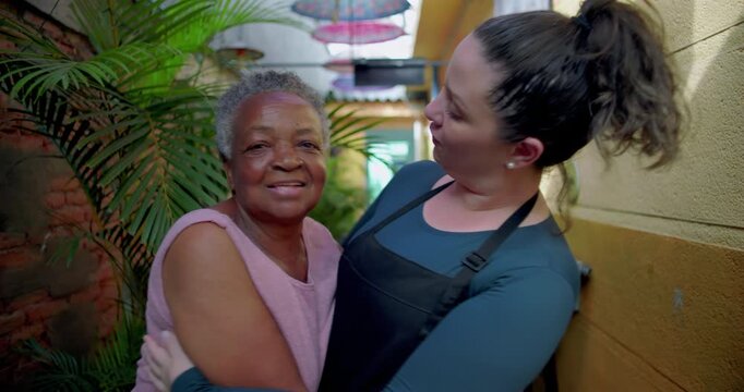 African American elderly woman warmly embraced by female server in outdoor corridor expressing care gratitude human kindness intergenerational bond and emotional connection