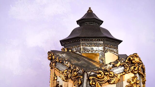 Detail of an ornate, decorative structure with dark roof and gold accents against a soft, textured background