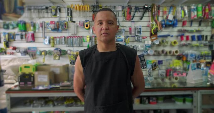 Hispanic hardware store worker standing among tools with serious expression conveying focus responsibility resilience and dignity of skilled manual labor