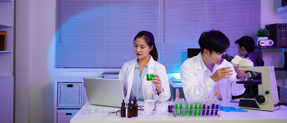 Asian Scientists Collaborating in Modern Lab, Two young asian scientists, a man and a woman work together in a modern laboratory setting, using a microscope and laptop to analyze data