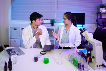 Asian Scientists Collaborating in Modern Lab, Two young asian scientists, a man and a woman work together in a modern laboratory setting, using a tablet and clipboard to analyze data