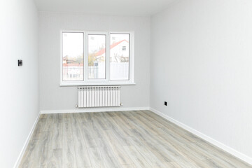 Obraz premium Empty interior room after renovations with white freshly painted walls and big window, allowing natural light, with a wooden floor, a radiator beneath the windows