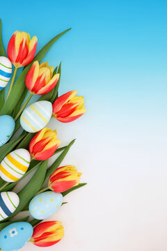 Easter egg, red yellow tulip flower seasonal background decoration on gradient blue white. Sweet candy treats with painted eggs for fun holiday season.