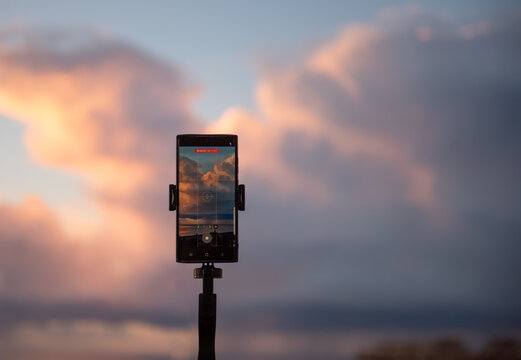 Mobile phone on tripod filming colorful clouds during twilight for travel content, vlog or tech promotion