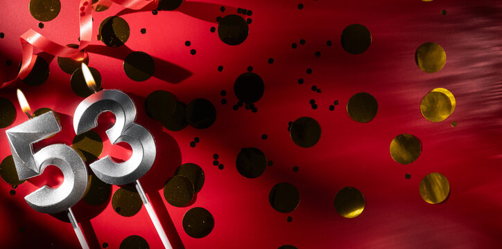 Concept of celebrating birthday and anniversary. Number 53 fifty-three silver celebration birthday candle on festive red background with large golden confetti. Fifty-three years birthday.