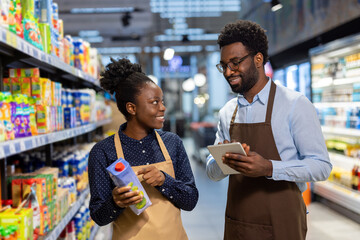 Supermarket employees are checking stock and discussing inventory in a grocery store aisle, using a digital tablet for efficient retail management and customer service