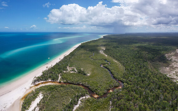 Aerial view of where the dark creek meets the azure bay waters, contrasting with the white sandy beach and dense green forest, Moon Point, K'Gari Fraser Island and Hervey Bay, Queensland, Australia.