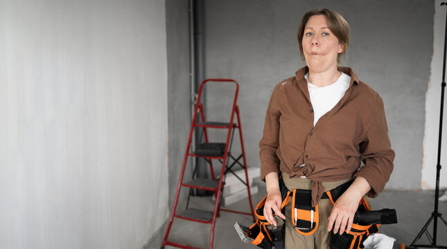 Funny woman in tool belt making fish face and comical expression during renovation.