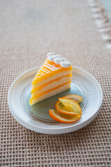 Delicious slice of orange fudge cake on a white plate.
Lifestyle food photography. The background is a cream-colored woven placemat.