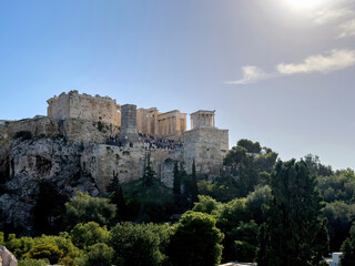 Obraz premium Acropolis of Athens and propylaea gate, visitors on the ruins, green trees, blue sky, view from Areopagus hill, Greece.
