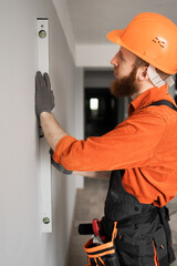 Portrait of bearded builder in hardhat measuring wall with spirit level