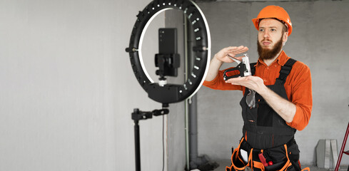 Bearded builder blogger in hardhat showing construction stapler on smartphone camera with ring light.