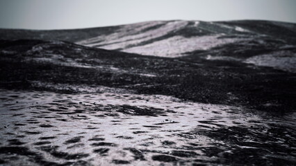 Fototapeta premium A vast volcanic terrain stretches out, displaying blackened earth and subtle patterns. The pale sky creates a stark contrast, enhancing the desolate beauty of this remote location.