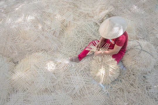 Aerial view of a woman in a conical hat meticulously crafting woven items amidst a sea of similar creations, Phan Ri Cua, Vietnam.