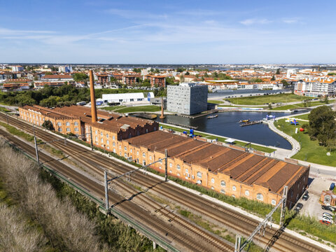 Aerial view of the contrasting textures of the old brick factory against the modern cube building by the still waters, framed by the city's skyline, Aveiro, Portugal.