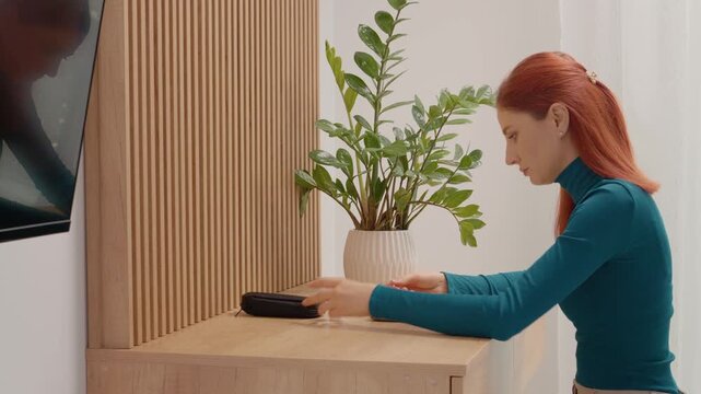 A woman sits at a table and takes a blood sugar test using a glucometer. She puts the test strip into the device to check her glucose level.