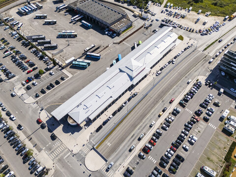 Aerial view of a bustling bus station bathed in sunlight, with rows of parked buses and cars creating a geometric pattern of transport, Aveiro, Portugal.