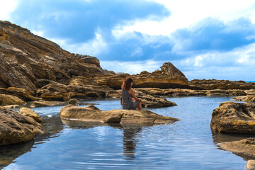 Fototapeta premium Woman sitting by tide pool on jaizkibel coast, enjoying solitude
