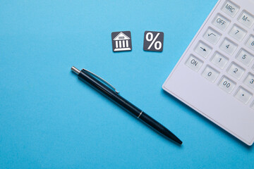 Percent and Bank symbol with a calculator and pen on the blue background.