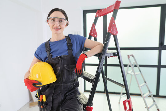 A skilled worker wearing a yellow hard hat and gloves takes a moment to pose near a ladder during an indoor renovation. The space is bright with a modern feel, showcasing dedication and focus.