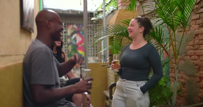 Friends continue conversation outdoors as one stands holding drink laughing openly conveying warmth ease and everyday social enjoyment