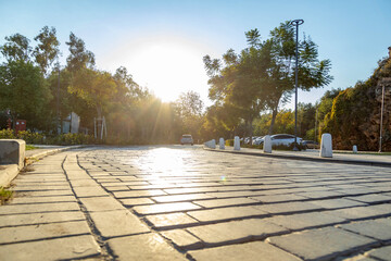 Bright backlight on a stone paved road in a city park at sunset. Low angle view of a cobblestone path under a glowing sun. Autumn evening in Konyaalti, Antalya, Turkey. October, golden hour light.
