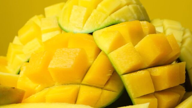 Juicy mango halves with cube cut pattern close-up rotation on yellow background